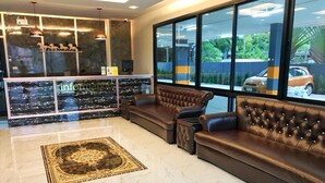 Eine moderne Lobby mit Marmorboden, Ledersofas, einer Rezeption und großen Fenstern mit Blick auf geparkte Autos.