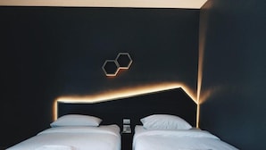 Ein Hotelzimmer mit dunkler Wand, einer sechseckigen Leuchte und zwei Betten mit weißer Bettwäsche.