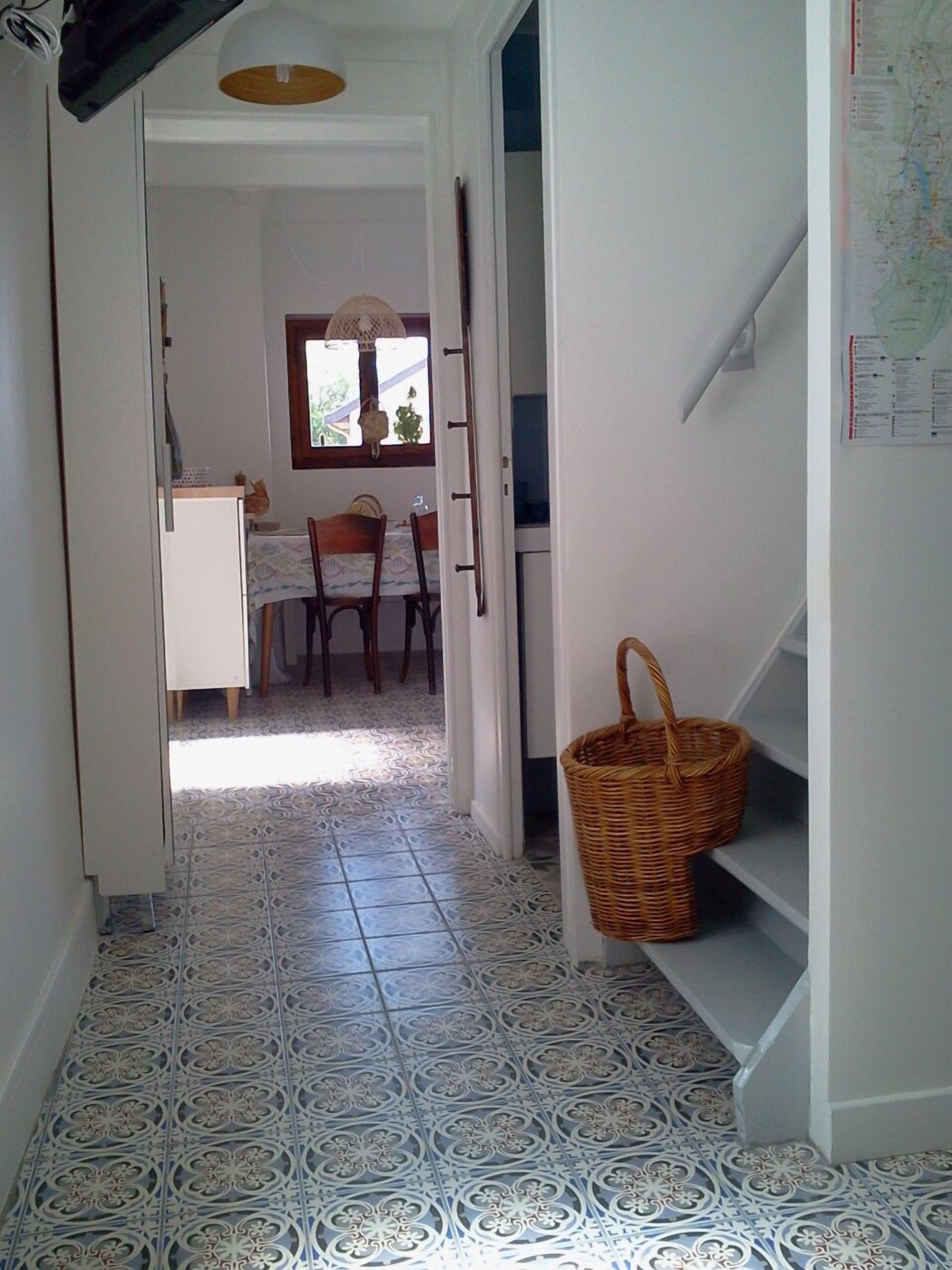 A hallway with patterned floor tiles, a dining area with chairs and a table, and a wicker basket on a shelf.