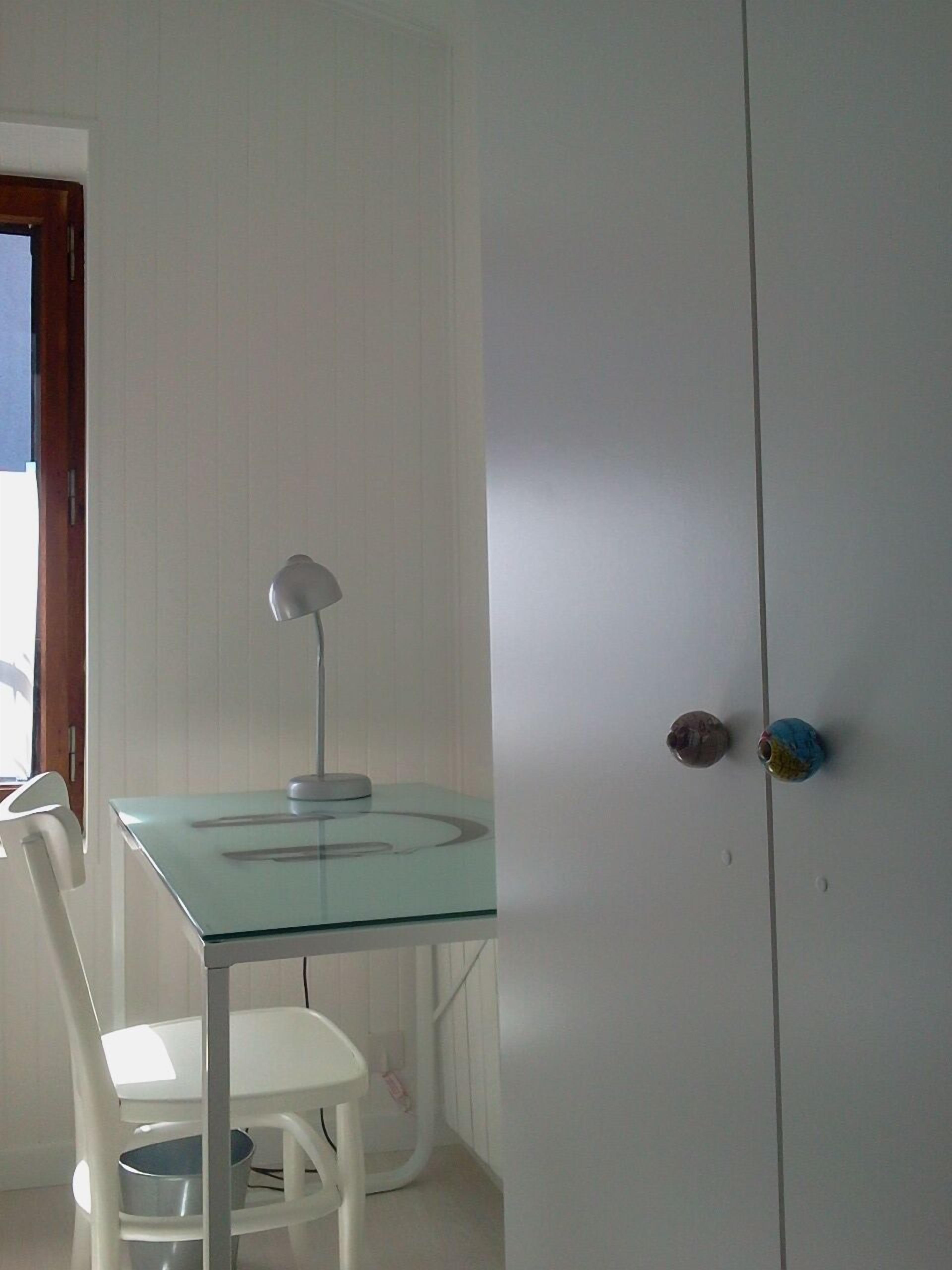 A room with a glass-top table, a white chair, a lamp, and a wardrobe with two doors.