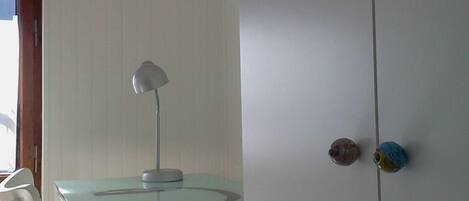 A room with a glass-top table, a white chair, a lamp, and a wardrobe with two doors.