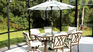 A glass-enclosed patio with a table and chairs, surrounded by greenery. - SUMMER SALE!!! - STUNNING VILLA, LARGE PRIVATE POOL & CONSERVATION VIEWS!! (Kissimmee)