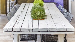 A rustic wooden table with chairs, a potted plant, and a kitchen area in the background. - Elisa Villa (Mylopotamos)