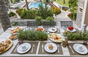 A dining table set for a meal with plates, cutlery, and glasses, surrounded by chairs and plants.