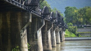 Eine Betonbrücke mit mehreren Pfeilern über einem Fluss, umgeben von Grünpflanzen und einer Steinmauer.