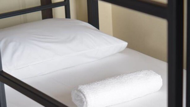 Ein Stockbett mit weißer Bettwäsche und einem zusammengerollten Handtuch.