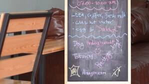 Eine Tafelauslage in einer Cafeteria mit einem Holzbstuhl und einer braunen Ledersitzbank im Hintergrund.