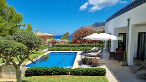 A pool area with a clear view of the ocean, a well-maintained lawn, and a patio with outdoor furniture. - Luxury design villa with fantastic sea and mountain views (Betlem)