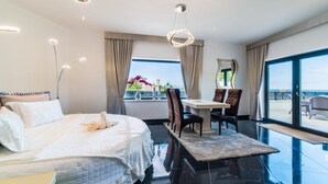 A modern hotel room with a large bed, a dining table with chairs, a balcony with outdoor seating, and a view of the sea. - Luxury design villa with fantastic sea and mountain views (Betlem)