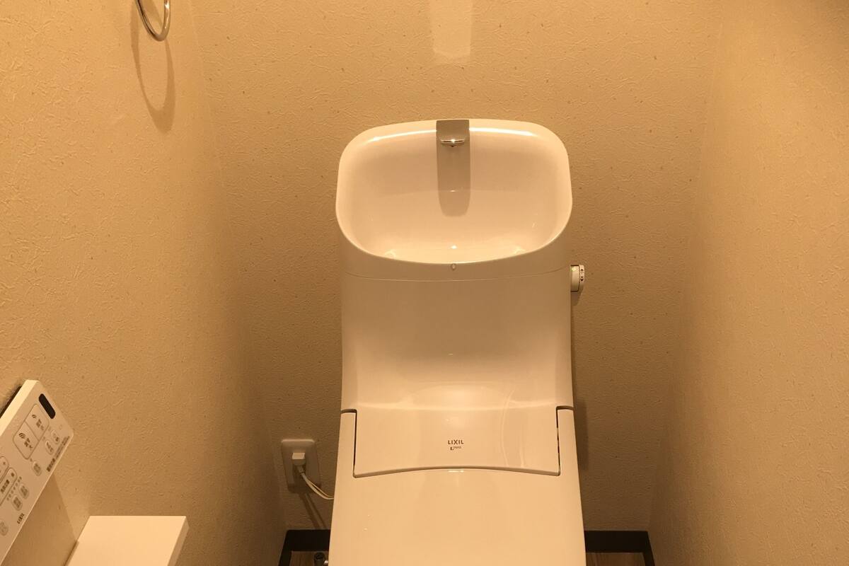 Ein kleines Badezimmer mit Toilette, einer weißen Wand, einem Holzboden und einer grünen Matte.