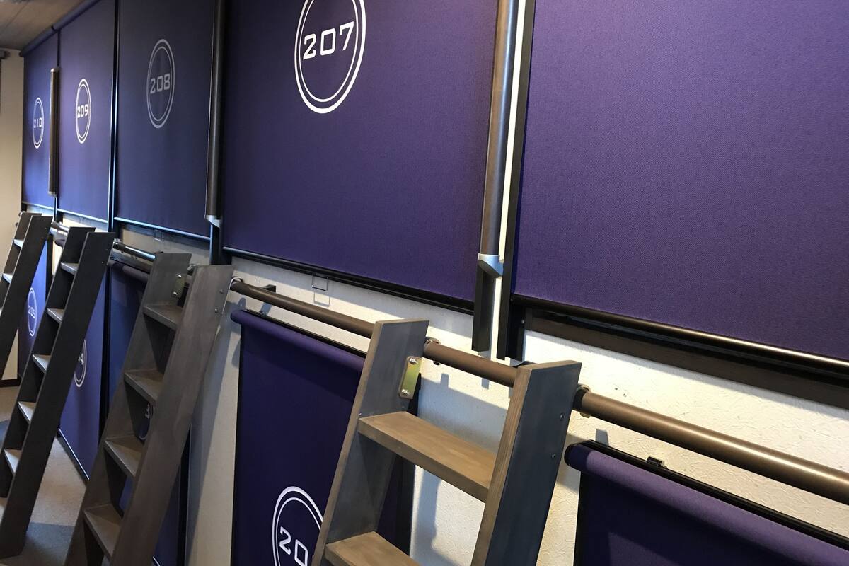 Eine Reihe von Hotelzimmern mit violetten Wänden und nummerierten Türen, jedes mit einem kreisförmigen Logo.