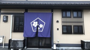 Eine Gebäudefassade mit einem schwarzen Tor, einem blauen Banner mit einem weißen Blumenmuster und einem Wasserspender auf der linken Seite.