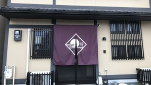 Une façade d’immeuble ornée d’une banderole violette sur laquelle figure un logo blanc, ainsi que de fenêtres à encadrement noir et d’un portail noir.
