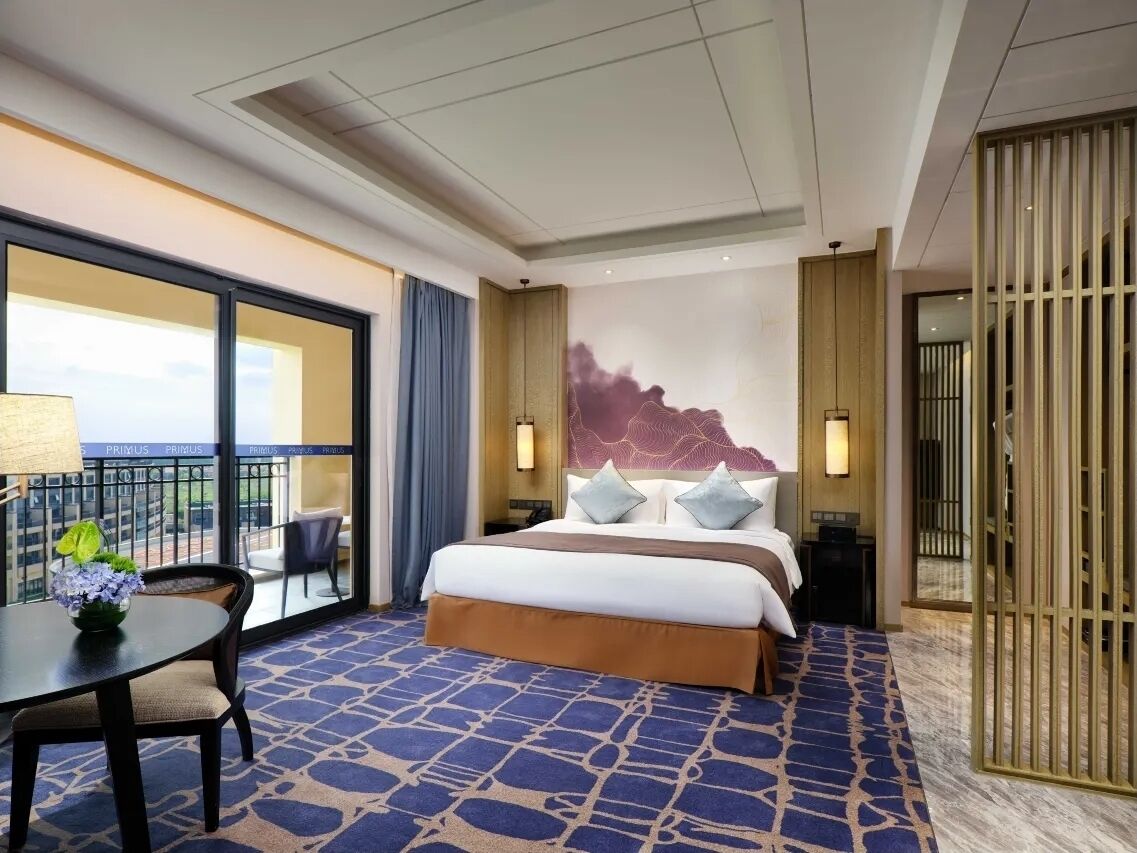 Ein Hotelzimmer mit einem großen Bett, einem Schreibtisch mit Lampe, Blick auf die Stadt und einer Wandverzierung.