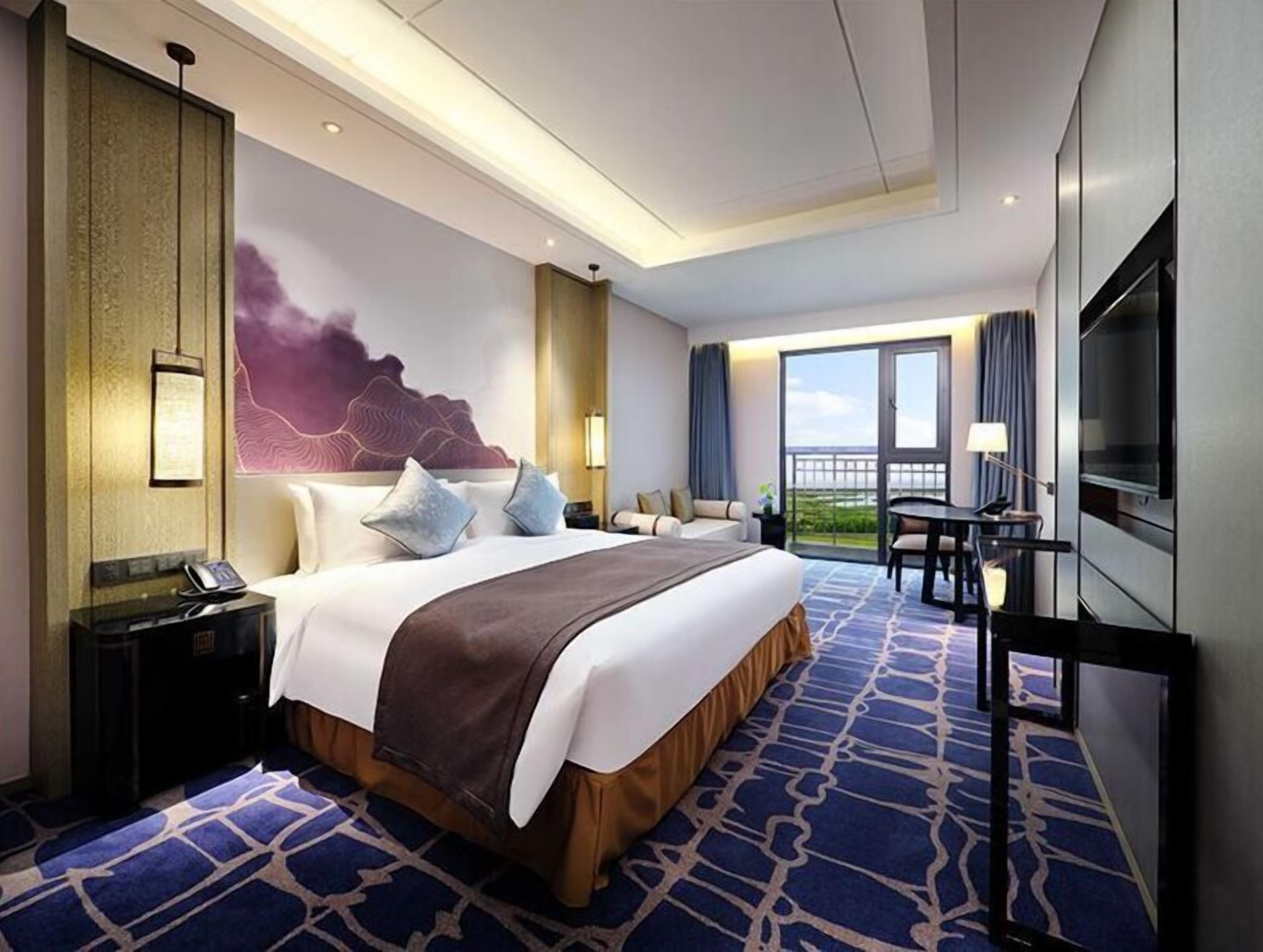 Ein Hotelzimmer mit einem großen Bett, einem Schreibtisch, einem Fernseher und einem Balkon mit Blick.