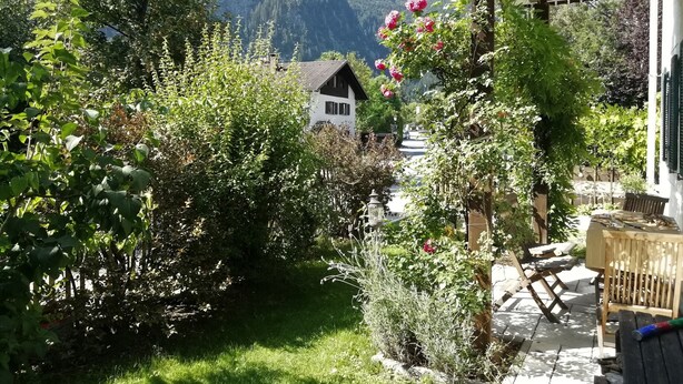 A garden with a wooden table and chairs, surrounded by greenery and a mountain view. - 'Sissi' a charming apartment in a modern country house style (Oberammergau)