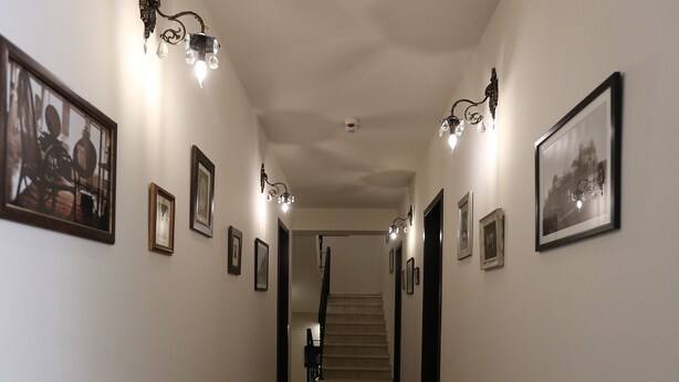 A hallway with framed pictures on the walls, a patterned carpet, and a staircase at the end. - Hotel Le Caucase (Tbilisi)