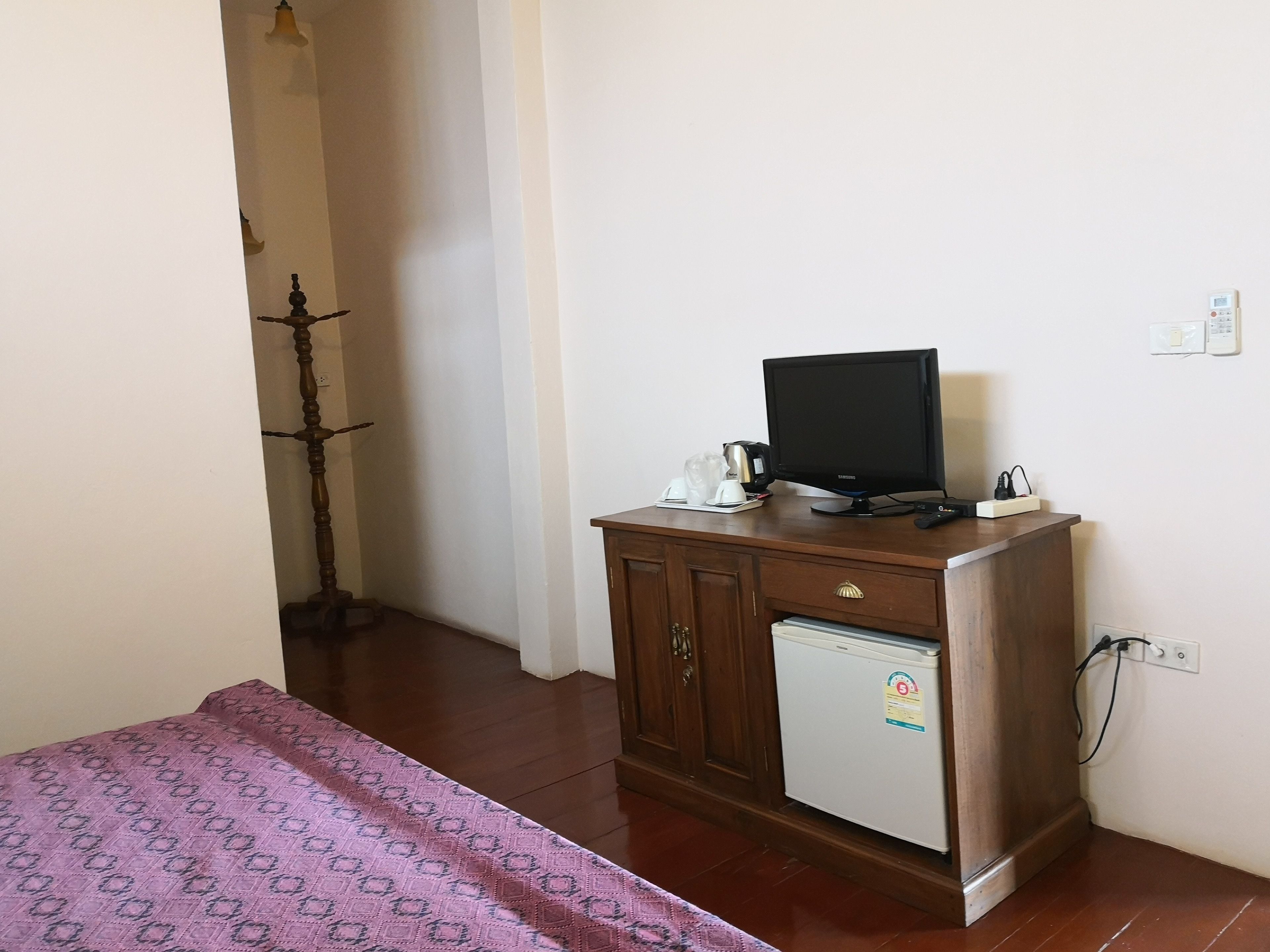 A small room with a wooden cabinet, a television, a refrigerator, and a patterned bedspread.