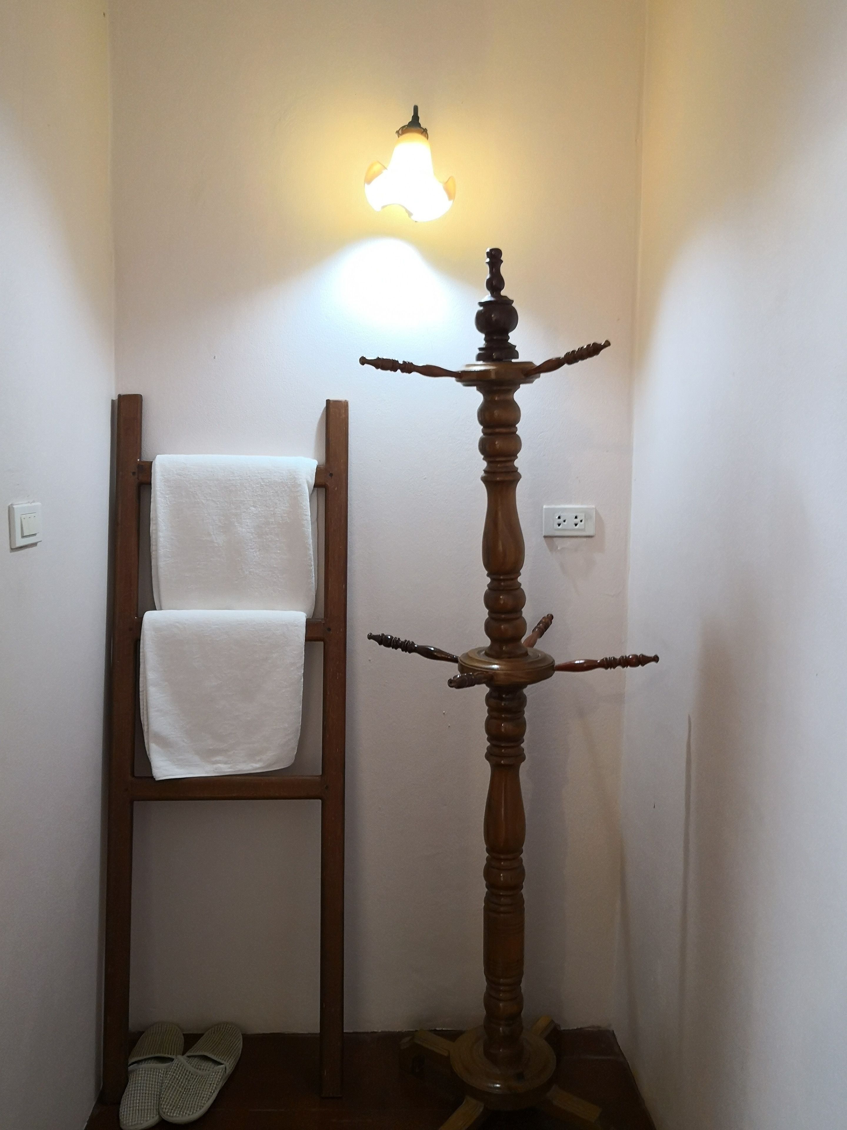 A wooden floor lamp with a light fixture, a wooden ladder leaning against a wall, and a pair of slippers on the floor.