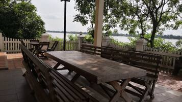 Un patio al aire libre con mesa y bancos de madera, rodeado por una valla blanca de piquetes, con vista a una masa de agua.