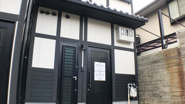 A traditional Japanese building with a black and white facade, two black doors, and a small sign on the right door. - One More Heart at Kamishichiken 2 (Kyoto)