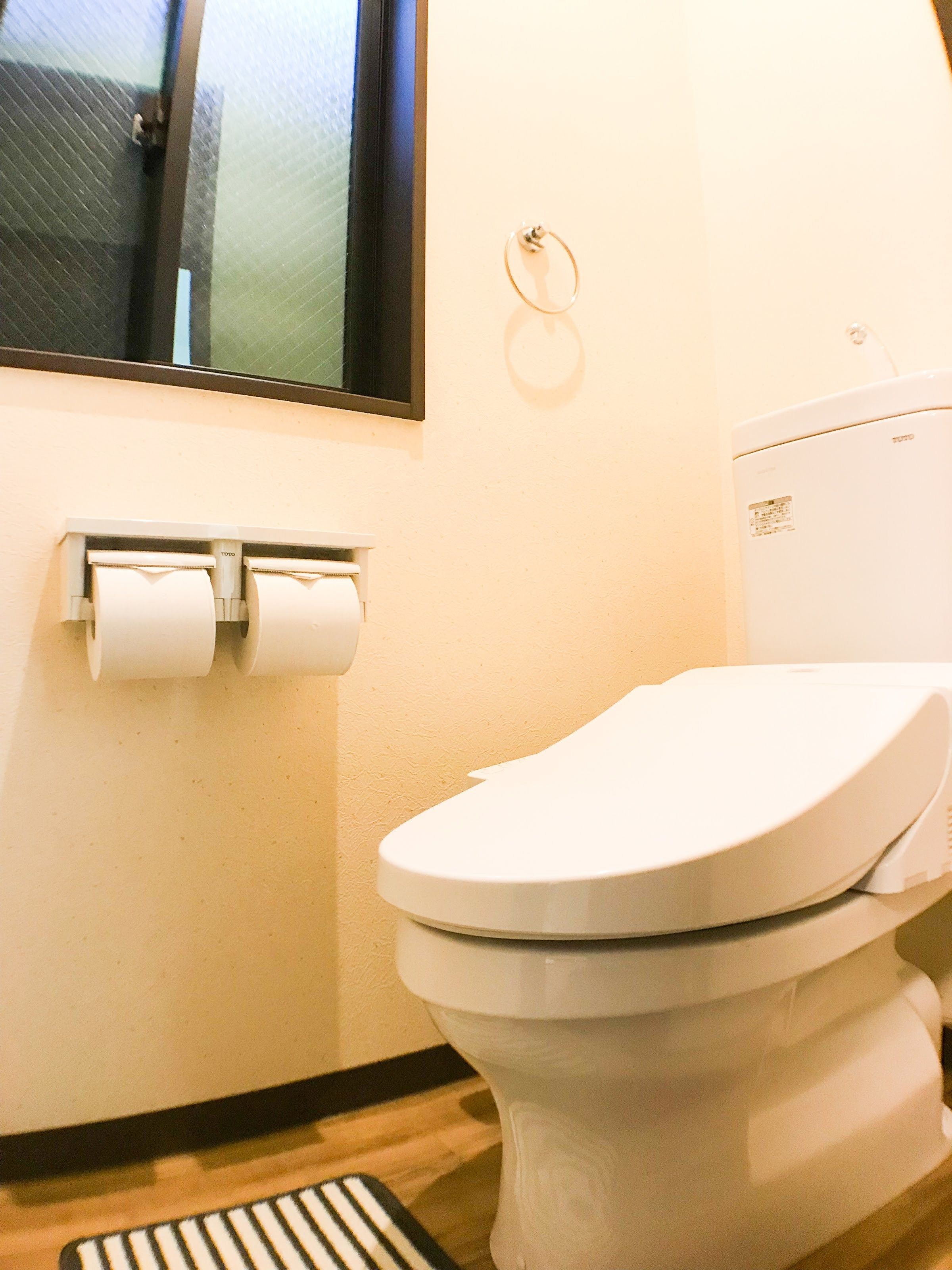 A toilet with a white seat and lid, a toilet paper holder with two rolls, and a window with a black frame.