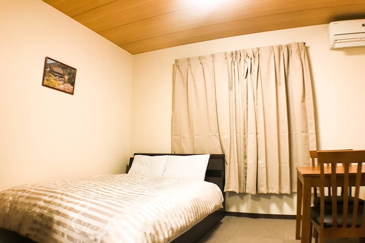 A bedroom with a bed, a chair, a window with curtains, an air conditioner, and a picture on the wall.
