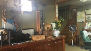 Ein traditioneller japanischer Raum mit Holzsitzmöbeln, einem Schreibtisch mit Computer, einem Fächer und verschiedenen Dekorationselementen, darunter eine Vase mit Blumen und ein gerahmtes Bild.