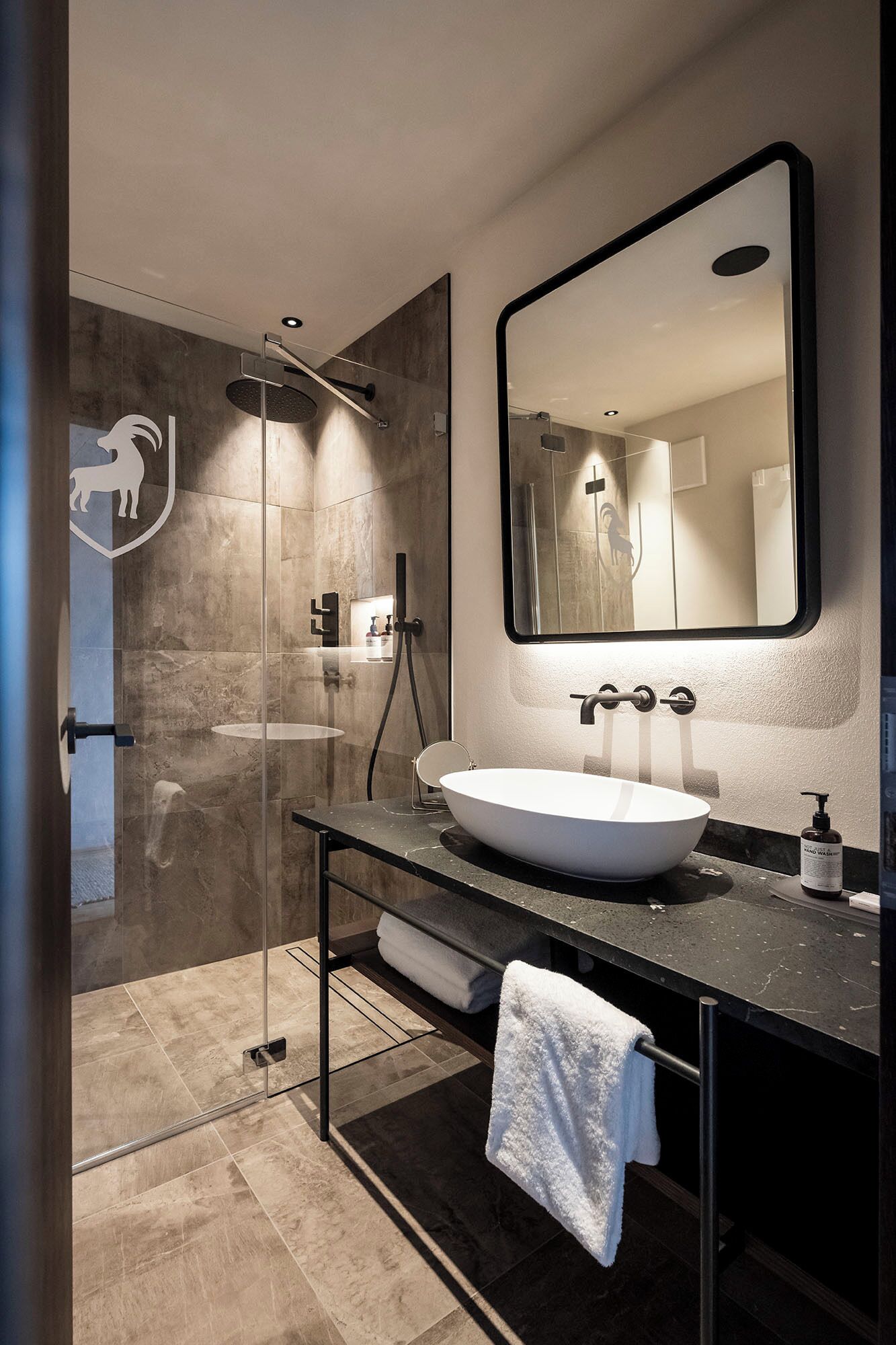 Ein modernes Badezimmer mit einer gläsernen Dusche, einem großen Spiegel und einem weißen Waschbecken.