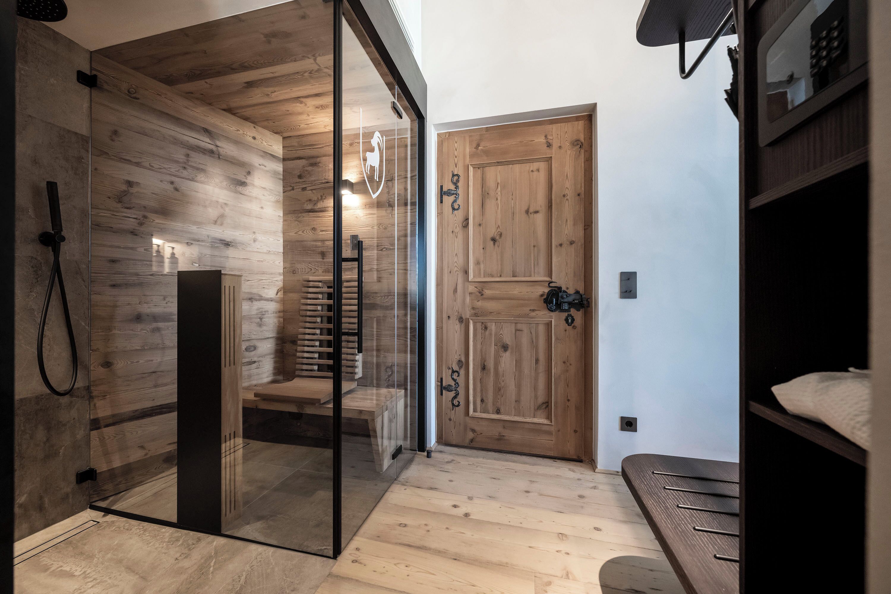 A modern bathroom with a glass shower enclosure, wooden flooring, and a wooden door.