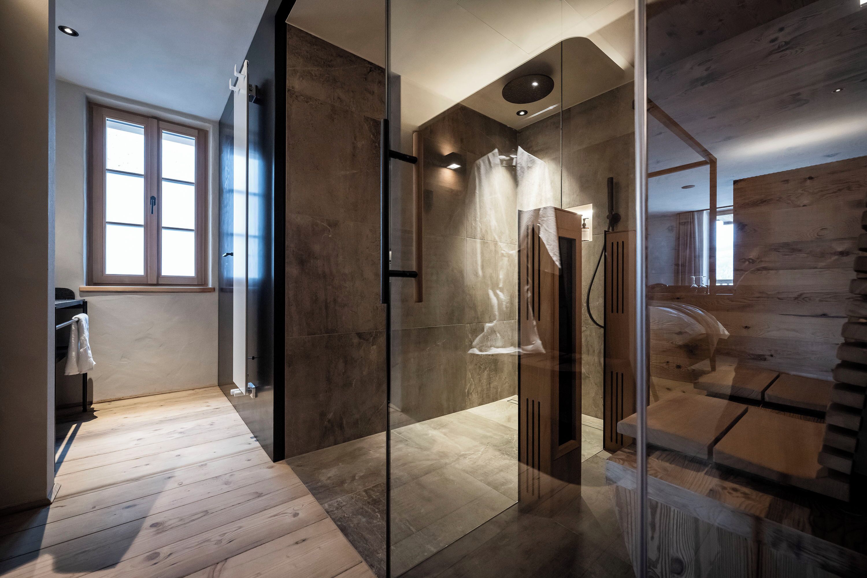 Un baño moderno con cabina de ducha de vidrio, suelo de madera y un ventanal que proporciona luz natural.