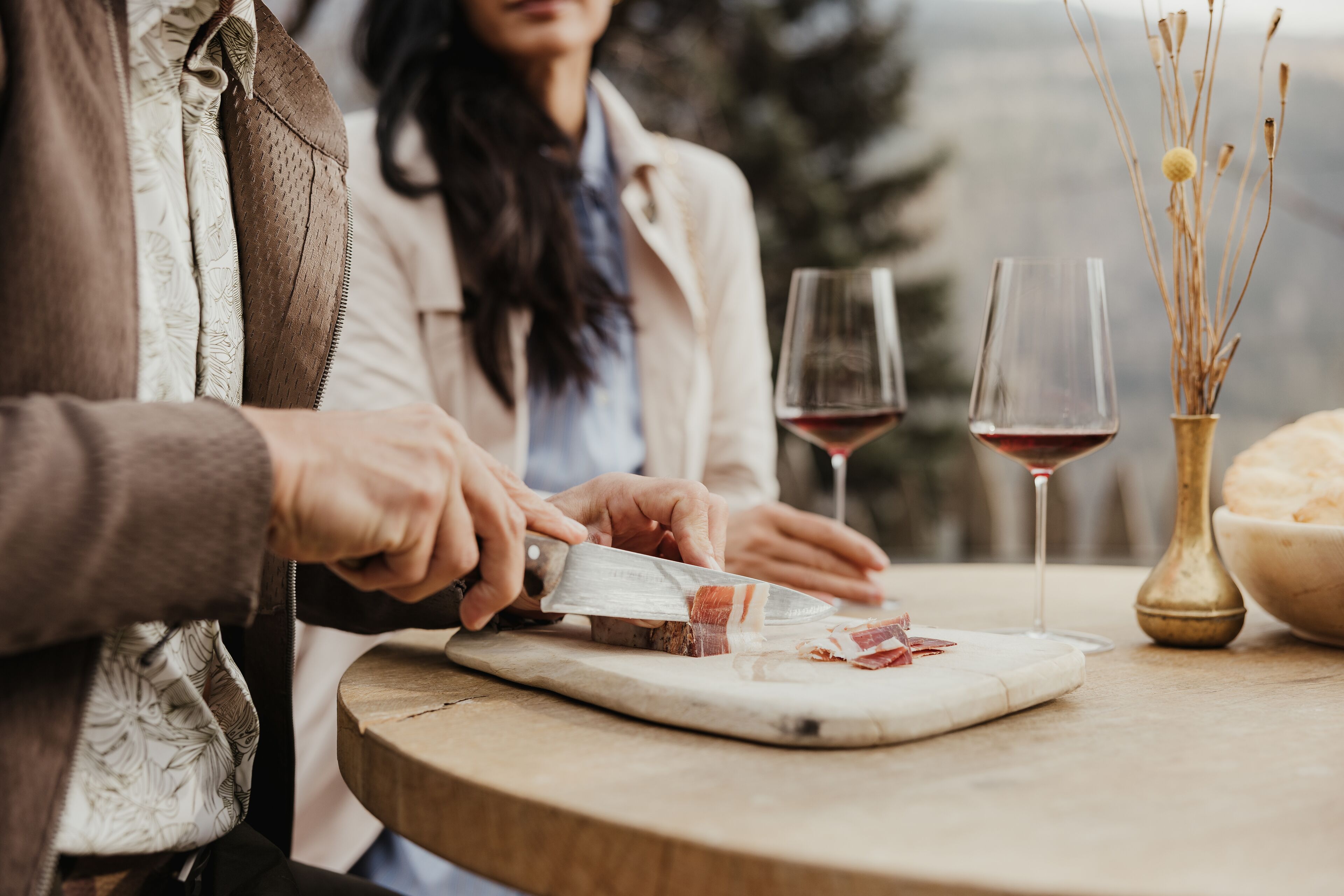 Una persona cortando carne en una tabla con dos copas de vino tinto sobre la mesa.