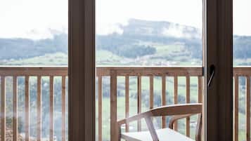 En træstol på en balkon med udsigt over et grønt landskab og fjerne bjerge.