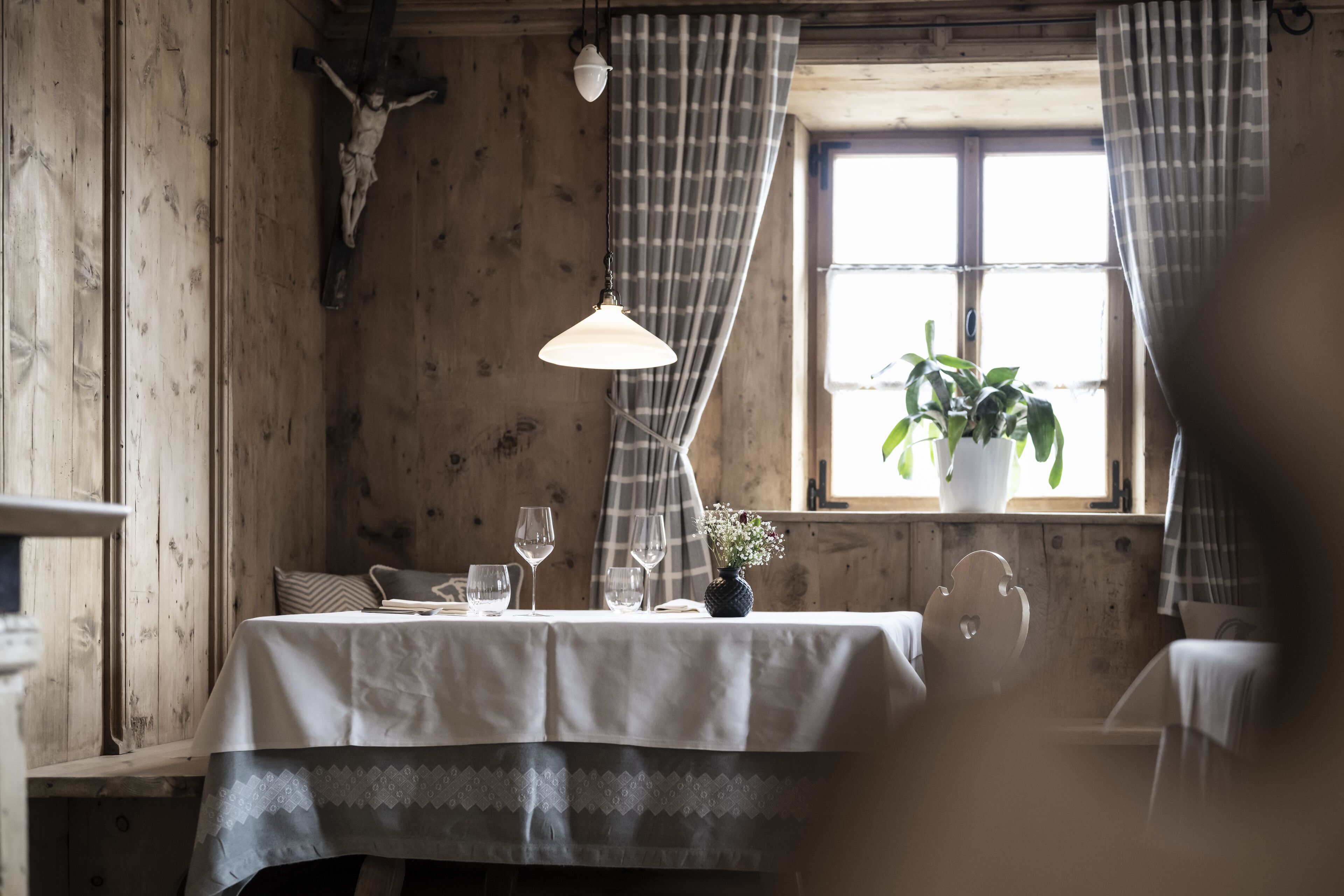 Un intérieur en bois avec une table dressée pour le repas, une plante en pot près de la fenêtre et une décoration rustique comprenant un crâne de vache.