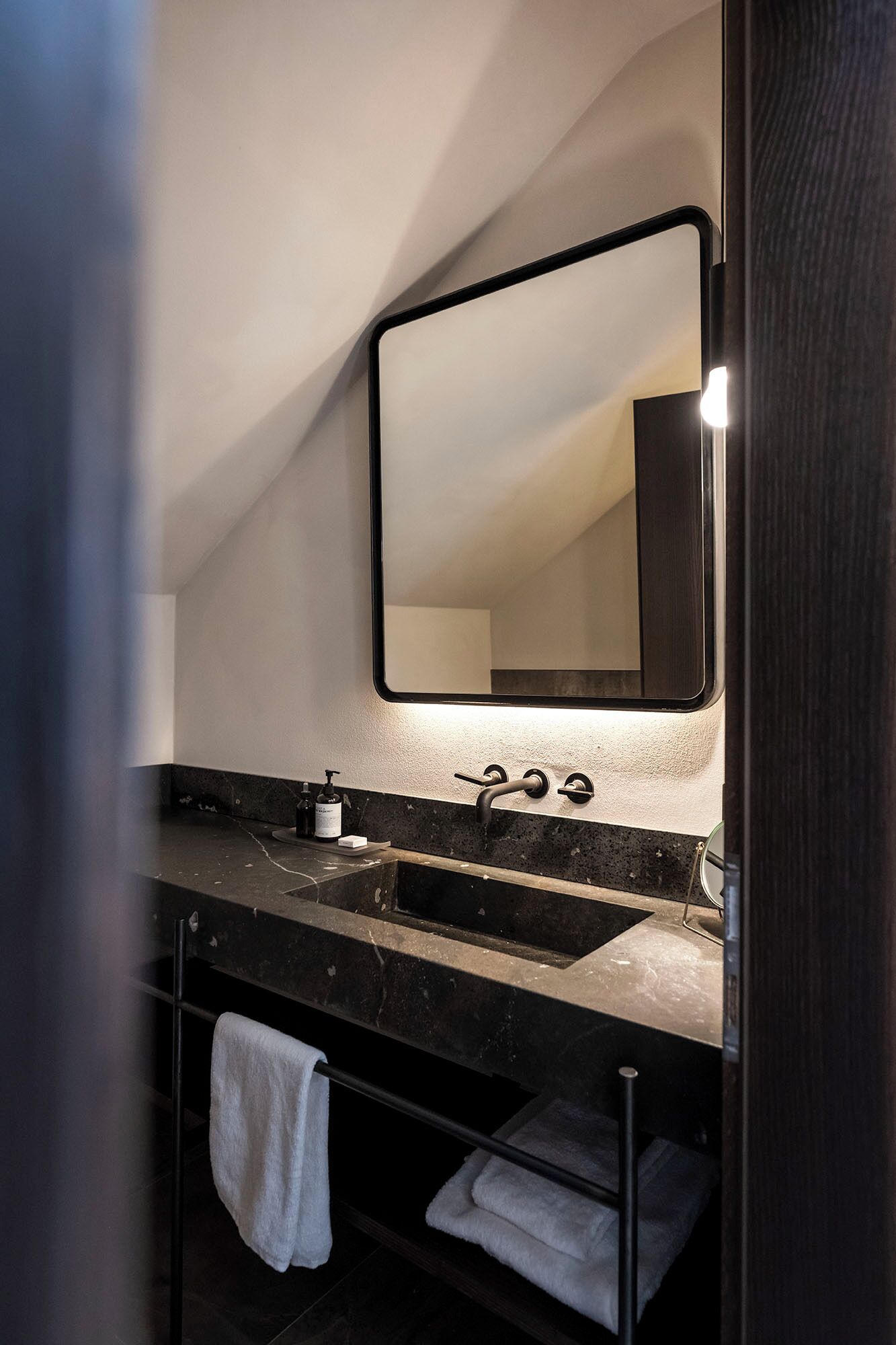 A modern bathroom with a dark marble countertop, a large mirror, and a towel rack.
