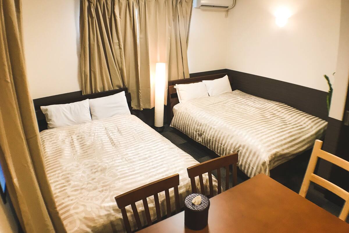 Une chambre d’hôtel avec deux lits, une table et une chaise. Il y a un climatiseur fixé au mur.