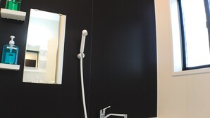 A modern bathroom with a black accent wall, a white bathtub, a handheld showerhead, a wall-mounted mirror, and a window providing natural light. - One More Heart at Fushimi Inari 3 (Kyoto)