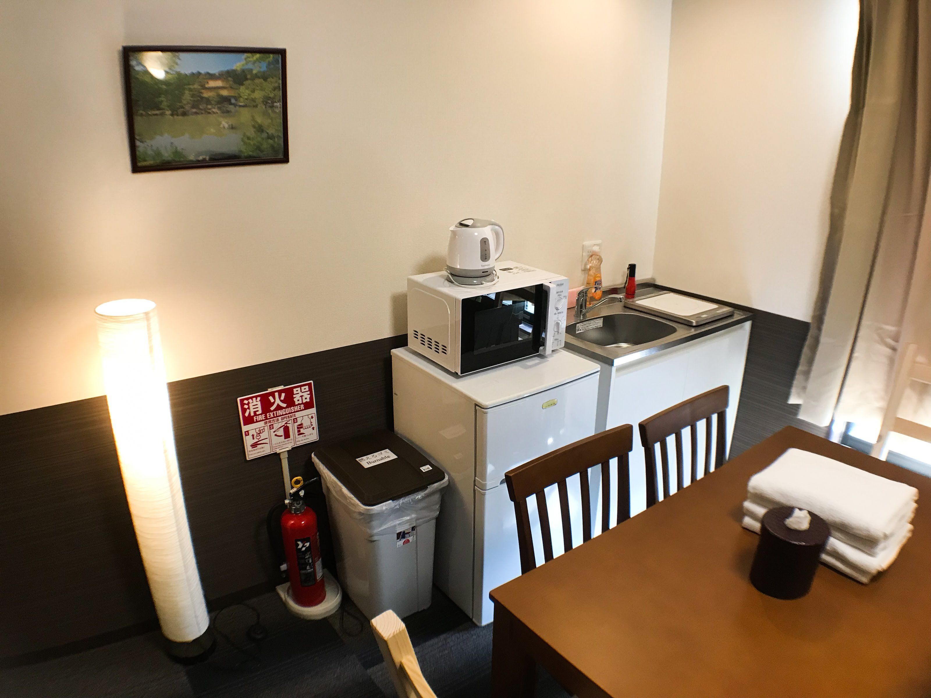 A compact kitchenette with a microwave, sink, and a small trash bin. There's a fire extinguisher on the floor and a sign indicating the location of the fire extinguisher.