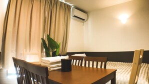 A hotel room with a wooden table, two chairs, a potted plant, a stack of towels, and an air conditioning unit on the wall. - One More Heart at Fushimi Inari 3 (Kyoto)