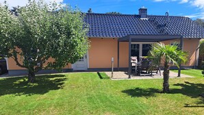 A house with a tiled roof, a covered patio, and a well-maintained lawn. - Modern holiday house, relax in the countryside on one level (Karlshagen)