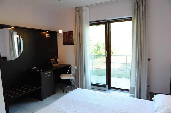 A hotel room with a bed, a desk, a chair, a large mirror, and a sliding glass door to the outside. - Country House Il Papavero (Bagnoli Irpino)