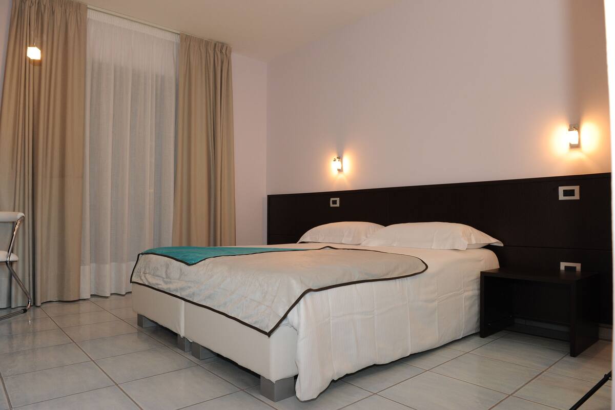 A hotel room with a bed, nightstands, a chair, and curtains.