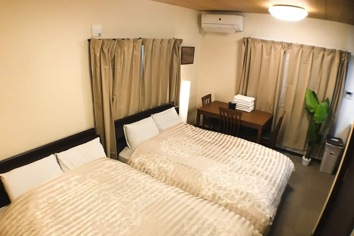 A hotel room with two beds, a desk, a chair, an air conditioner, and a trash bin.