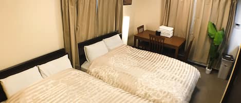 A hotel room with two beds, a desk, a chair, an air conditioner, and a trash bin.