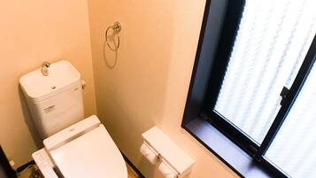 A small, compact bathroom with a toilet, a toilet paper holder, a window, and a vent.