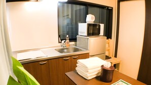 A compact kitchen with a microwave, sink, and a small table with a tissue and a menu. - GH One More Heart at Toji 2 (Kyoto)