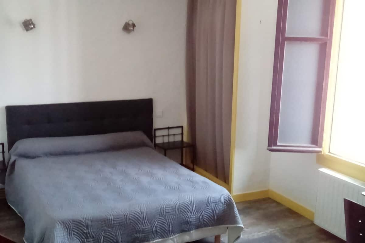 Ein Einzelbett mit dunklem Kopfteil in einem Zimmer mit Fenster und Vorhang.