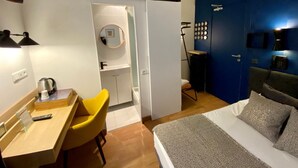 A compact hotel room with a bed, a desk with a chair, a small bathroom, and a blue accent wall. - Hôtel Les Beaux Arts (Limoges)