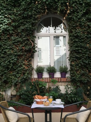 A table set for breakfast with croissants, juice, and coffee, surrounded by ivy-covered walls and a window with potted plants. - Hôtel Les Beaux Arts (Limoges)