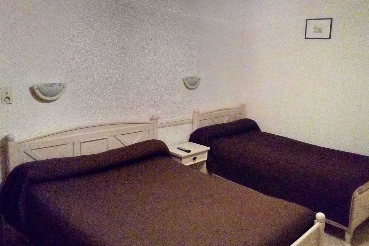 Ein kleines Zimmer mit zwei Einzelbetten, einem Nachttisch mit Lampe sowie einer Wandleuchte.